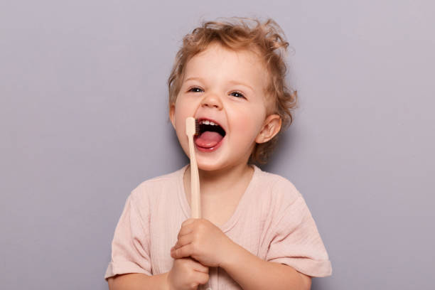 a little kid holding a toothbrush while smiling widely