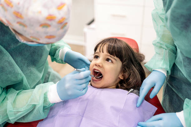 a little kid receiving dental check-up with her dentist and a dental assistant