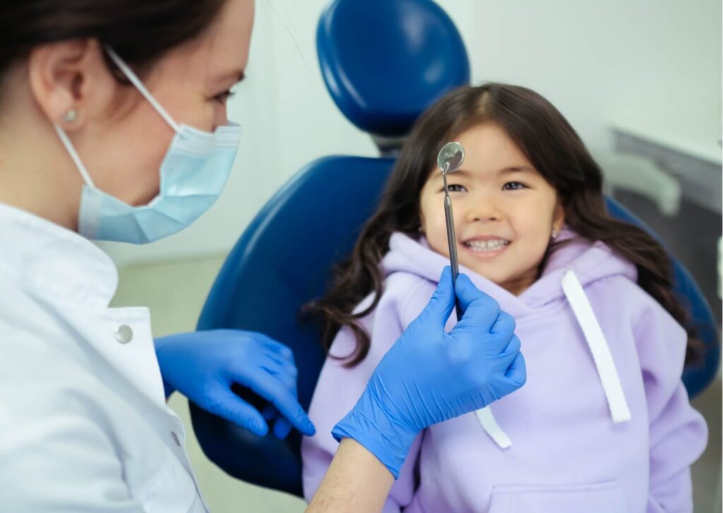 Pediatric dentist showing a dental mirror to a young patient before discussing a kids dental spacer and preventive care.