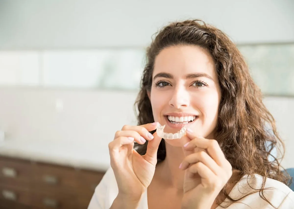 Woman holding a clear retainer used to keep teeth in their corrected positions after braces or aligners.